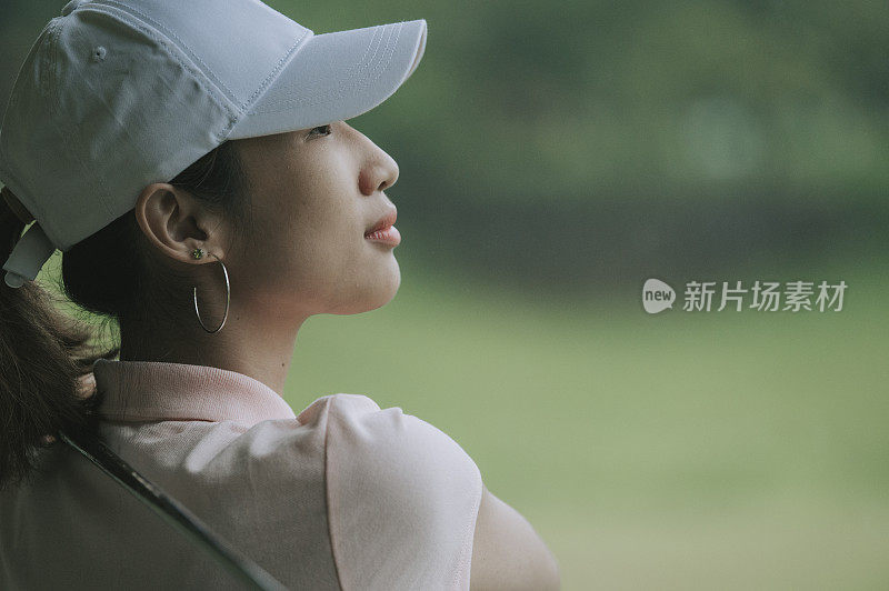 asian chinese young female golfer swing her driver at golf driving range in rain